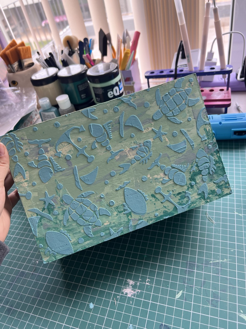 Una caja de cartonaje pintada en verde agua, con tortugas, peces y estrellas de mar en relieve