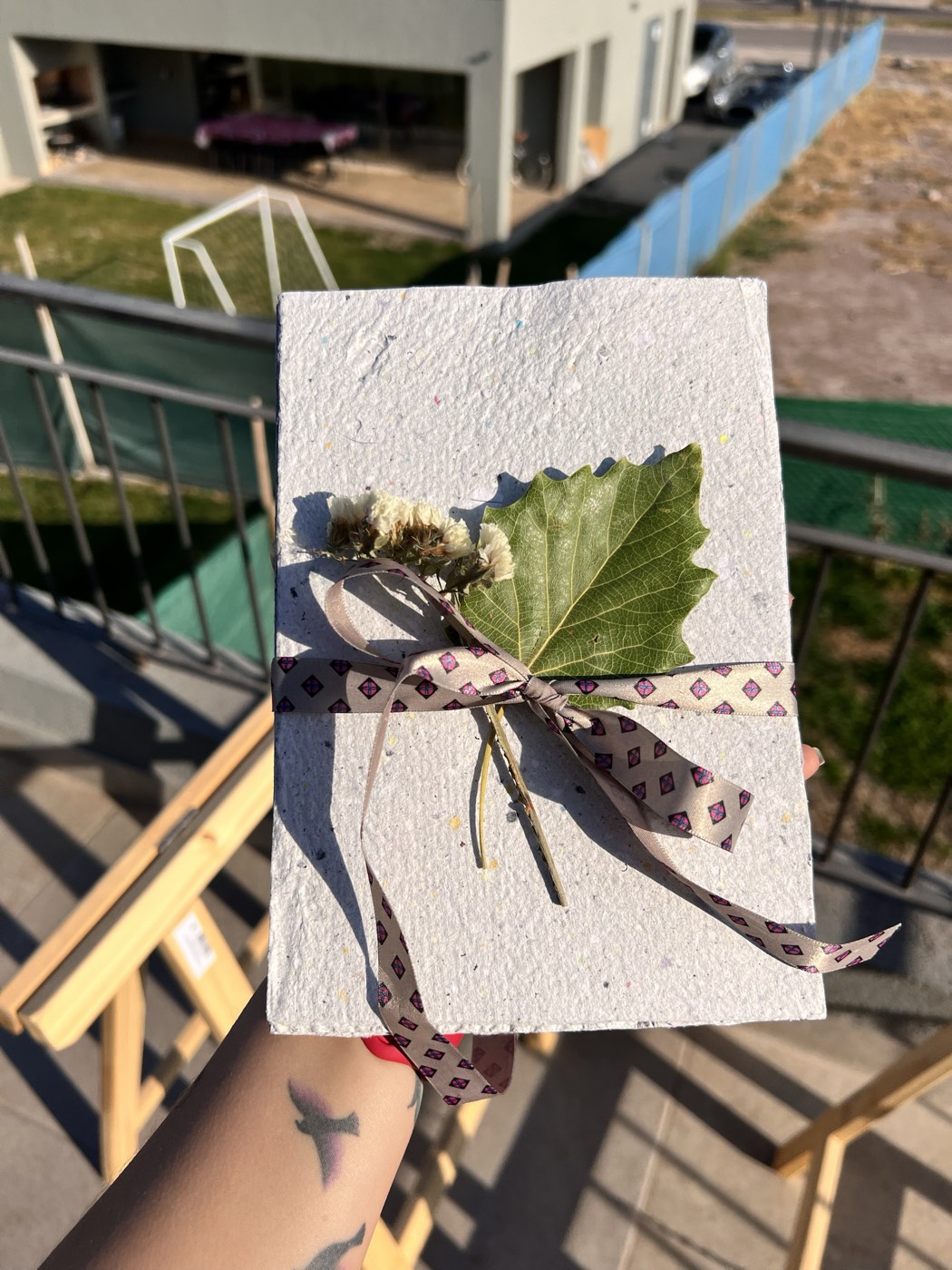 Una tarjeta hecha con papel reciclado que hizo ella misma, con una hoja verde y flores secas, atada con una cinta