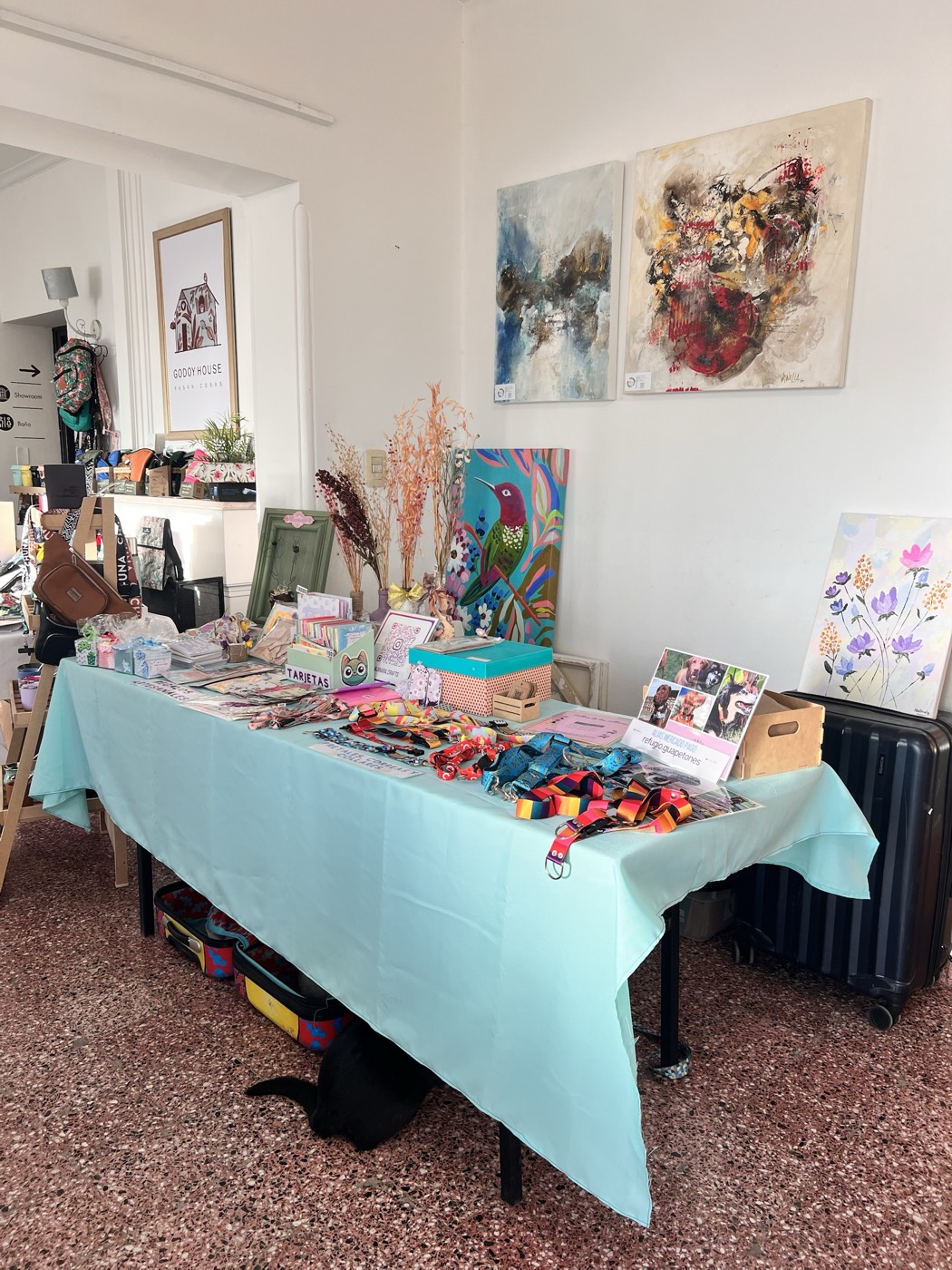 La mesa de Jinara Crafts en una feria de Mendoza: mantel turquesa, tarjetas, el QR de la cuenta y los collares de Guapetones