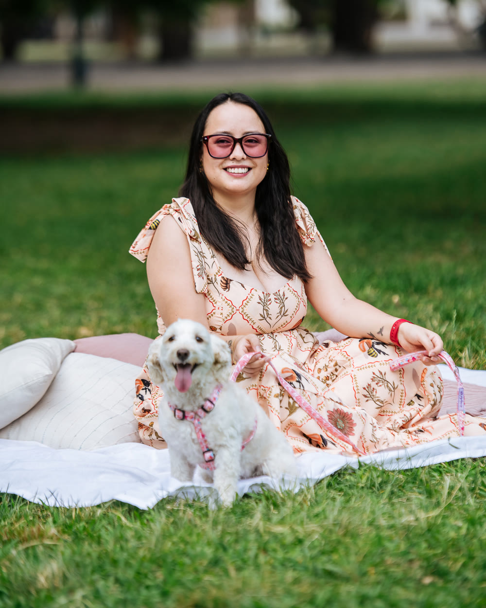 Nath sentada en el pasto de un parque, sonriendo, con un perro blanco al lado