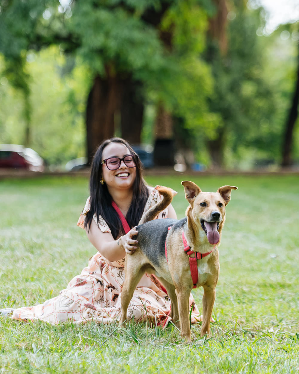 Nath sentada en el pasto de un parque, riéndose, con un perro marrón al lado