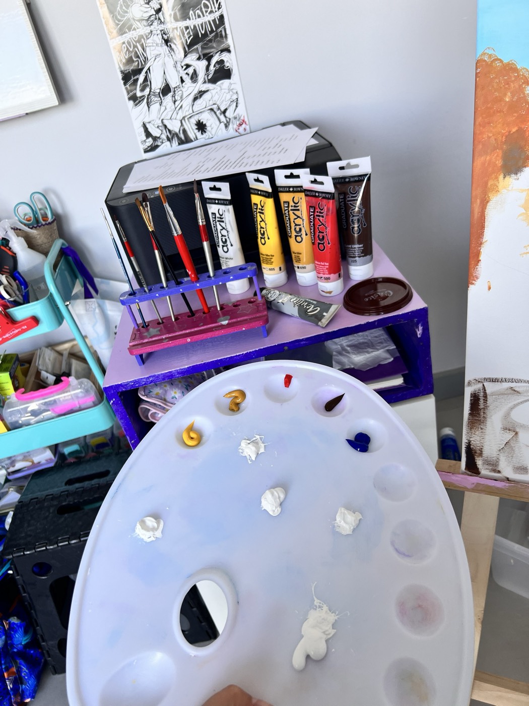 La paleta de pintura con acrílicos servidos, los tubos Daler-Rowney y los pinceles en un soporte pintado a mano